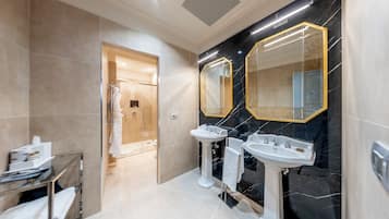 Un baño moderno con dos lavamanos, cabina de ducha de vidrio y paredes de mármol.