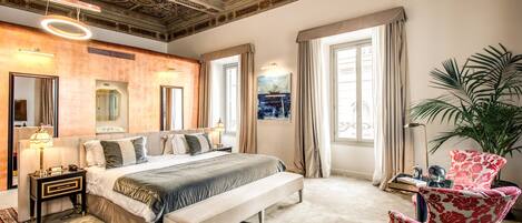 A bedroom with a large bed, a bench, a chair, a potted plant, and a painting on the wall.