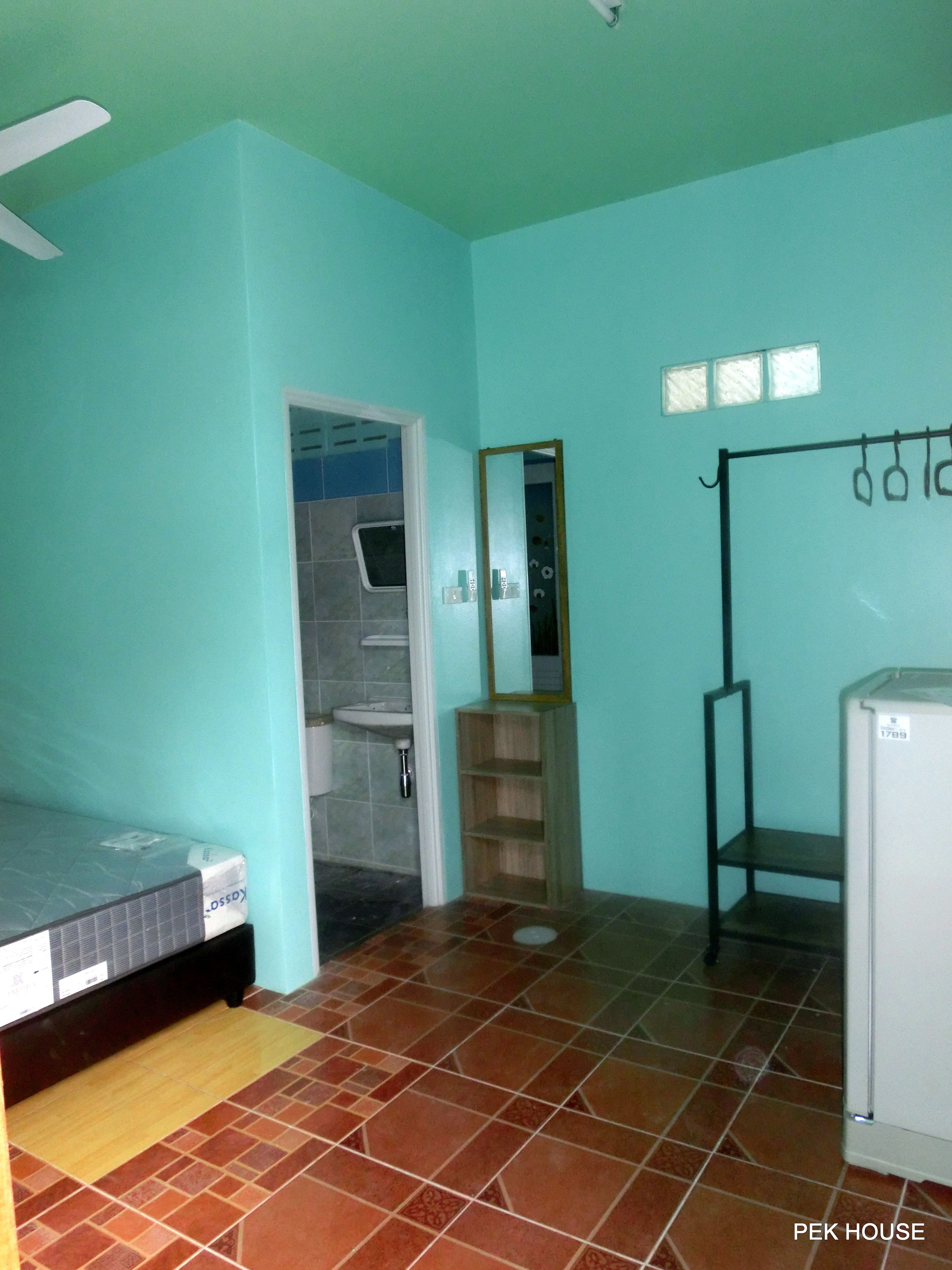 A room with teal walls, a tiled floor, a bed, a sink, a mirror, and a small refrigerator.