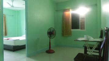 Una habitación con cama, ventilador, mesa y silla, y ventana con cortinas.