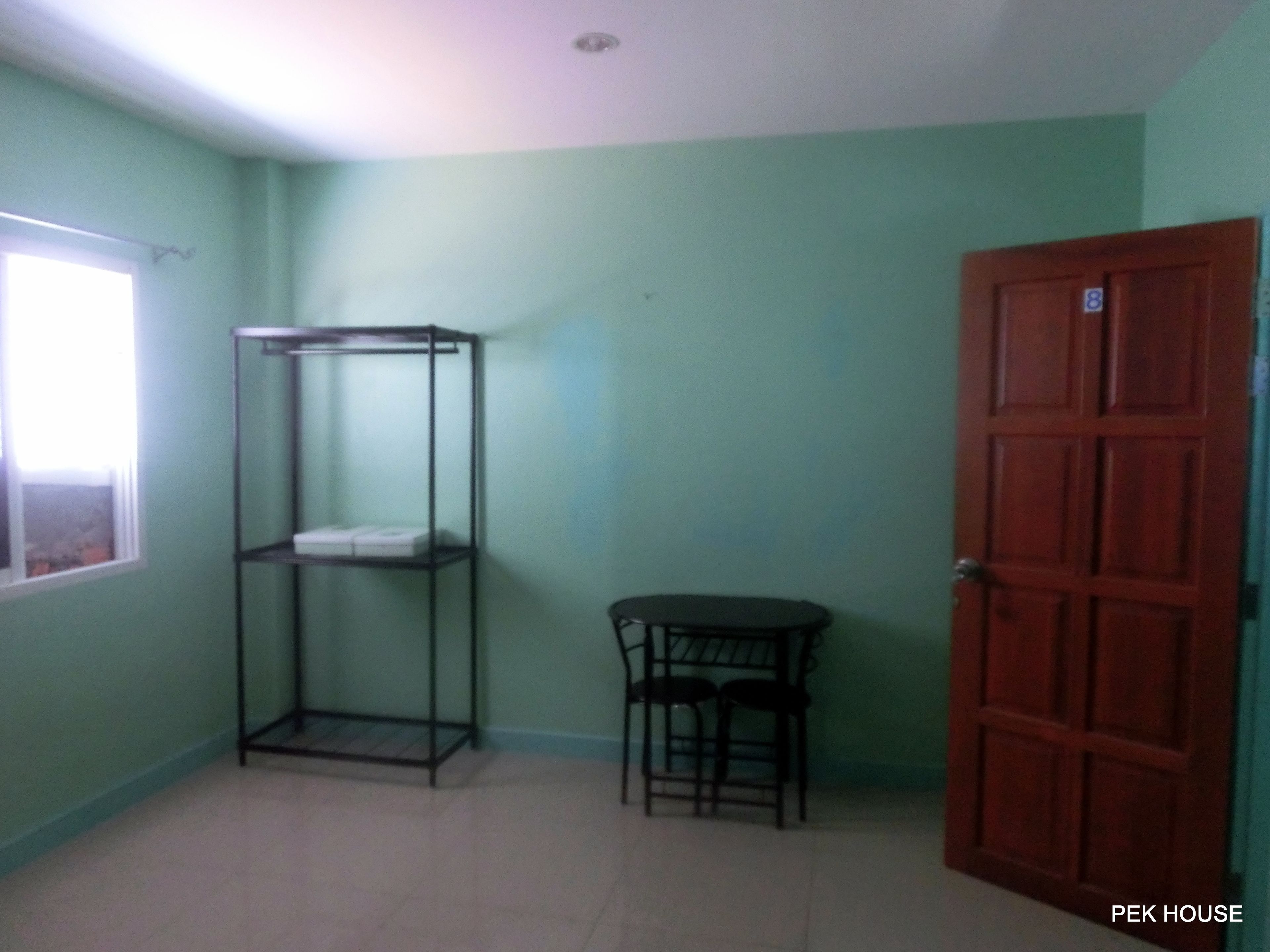 Una habitación con una estantería metálica, una pequeña mesa con dos sillas y una puerta de madera.
