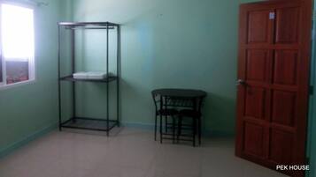 Una habitación con una estantería metálica, una pequeña mesa con dos sillas y una puerta de madera.