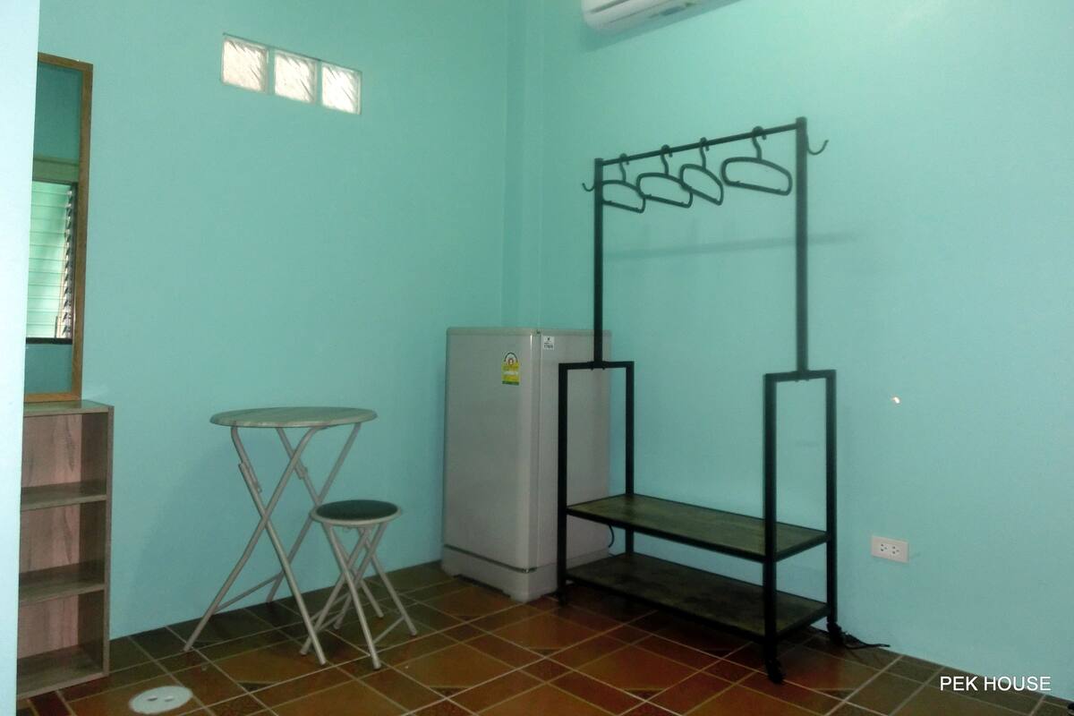 Une petite pièce, de dimensions réduites, aux murs de couleur turquoise, dotée d’un sol carrelé, d’une petite table avec un tabouret, d’un réfrigérateur et d’une étagère en métal.