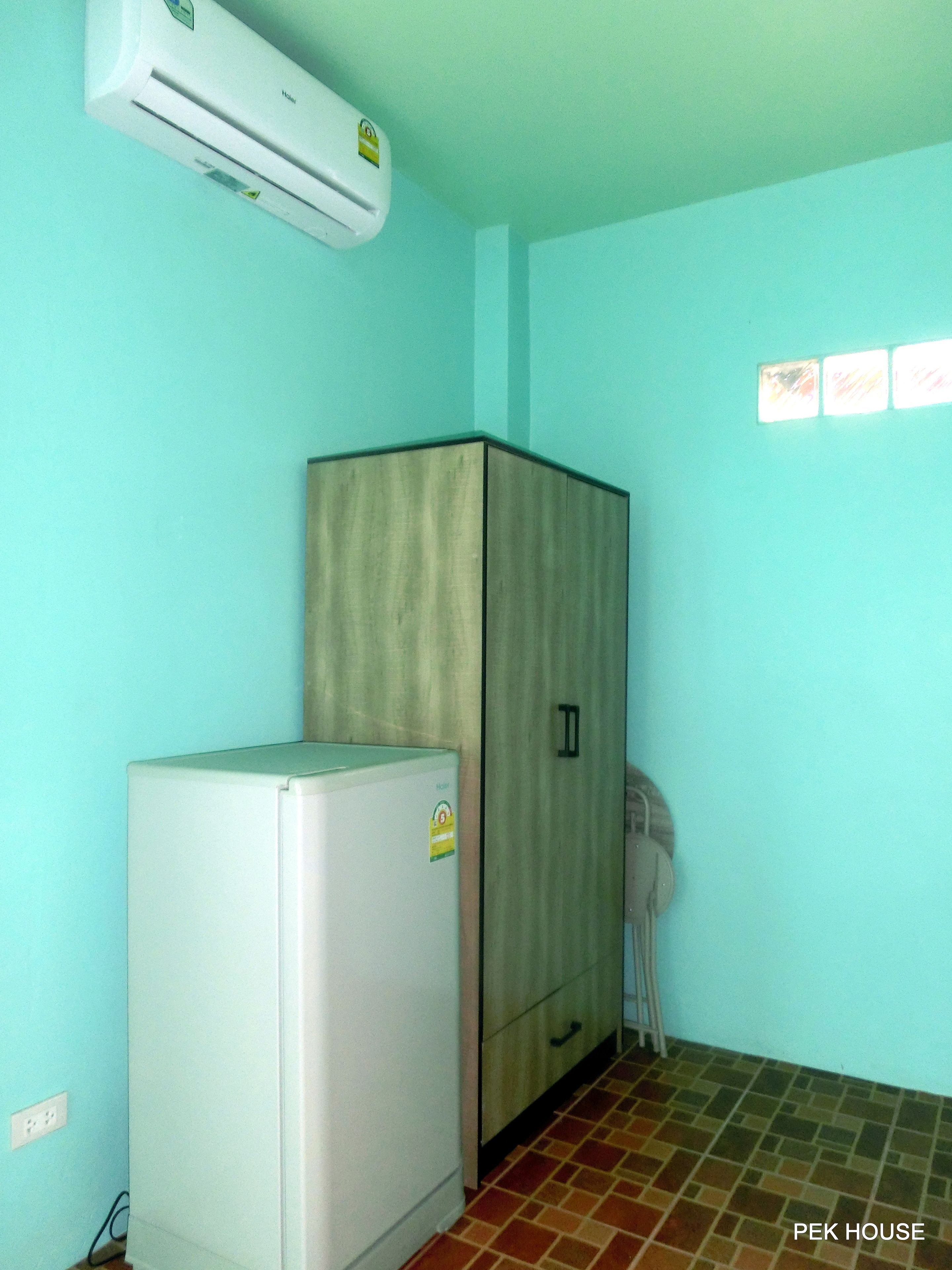 A small room with a white refrigerator, a wooden cabinet, and a wall-mounted air conditioner.