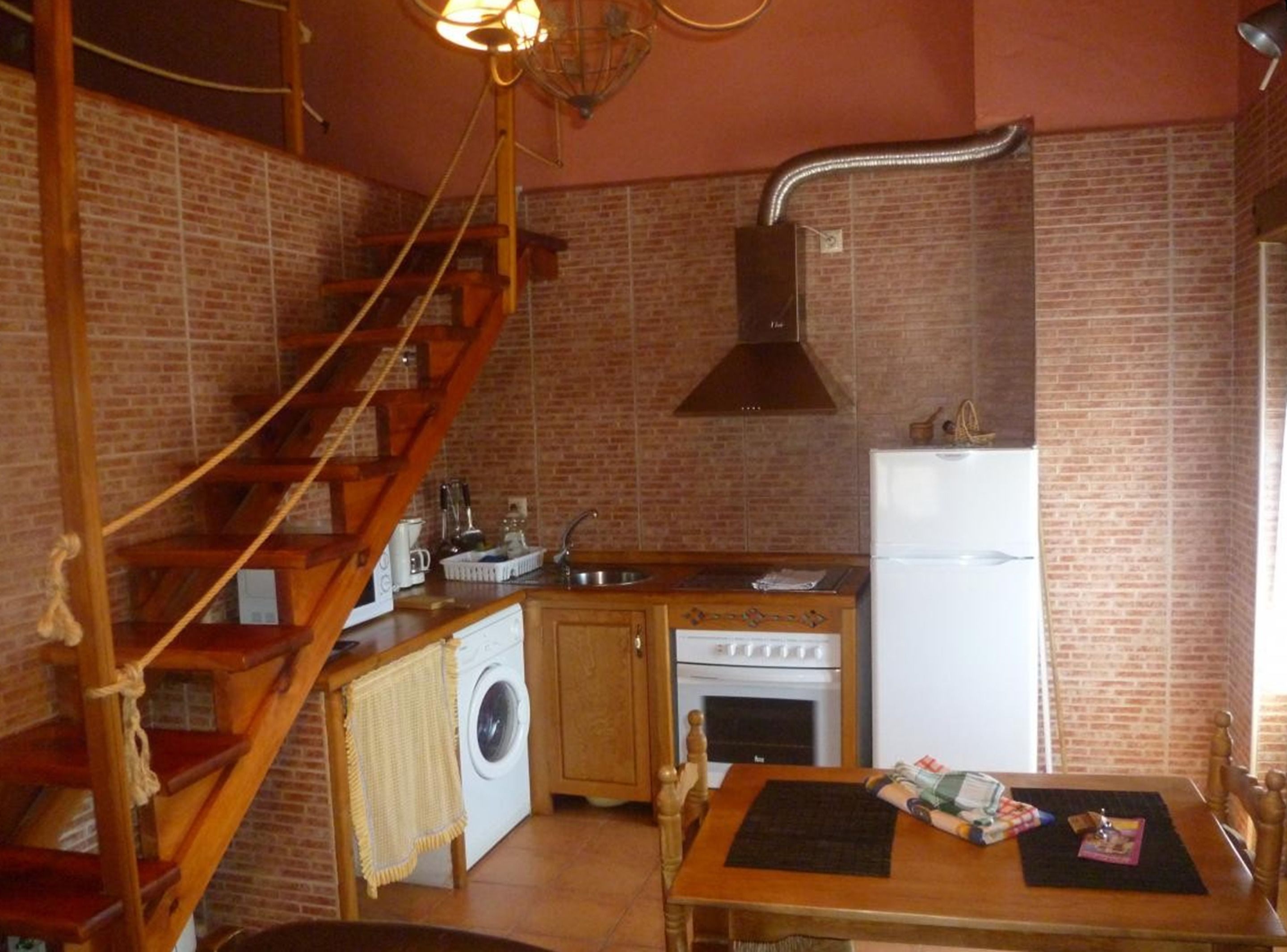 A compact kitchen with a wooden staircase, a washing machine, a stove, and a refrigerator.