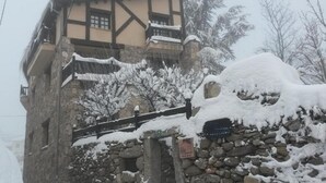 A traditional stone building with a wooden balcony and snow-covered surroundings. - Artesano III (Navarredonda de Gredos)