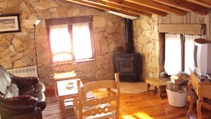 A cozy living room with a stone wall, wooden beams, a fireplace, a leather chair, a wooden table, and a television. - Artesano III (Navarredonda de Gredos)