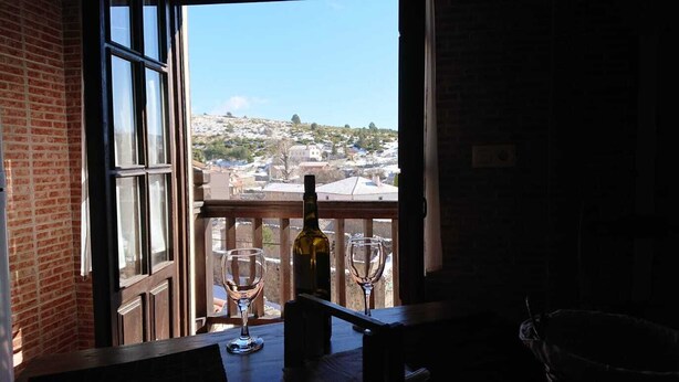A balcony with a view of a hillside town, a bottle of wine, and two wine glasses. - Artesano III (Navarredonda de Gredos)