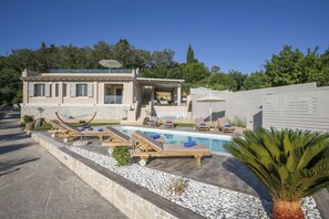 Una villa moderna con piscina, mobiliario exterior y un sendero de piedra.