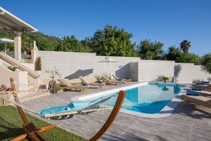 Zona de piscina con sillones reclinables y una hamaca.