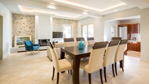 Un'ampia sala da pranzo con un grande tavolo in legno e sei sedie, un muro in pietra con un quadro e una cucina moderna sullo sfondo.