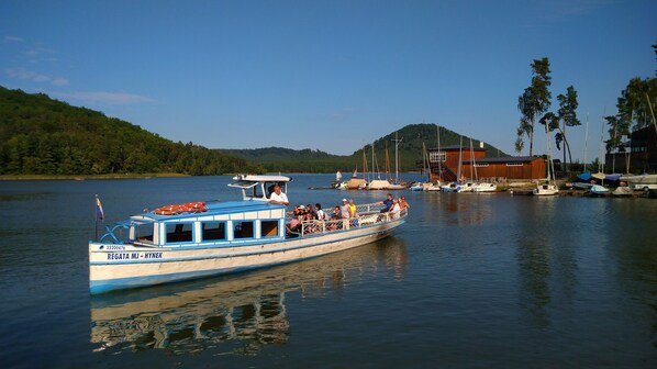 A boat with passengers, docked near a building with a hill in the background.