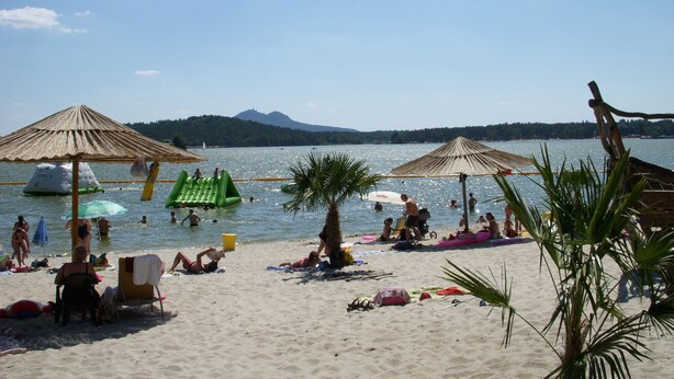 Una playa con sombrillas, gente tomando el sol y un lago tranquilo.