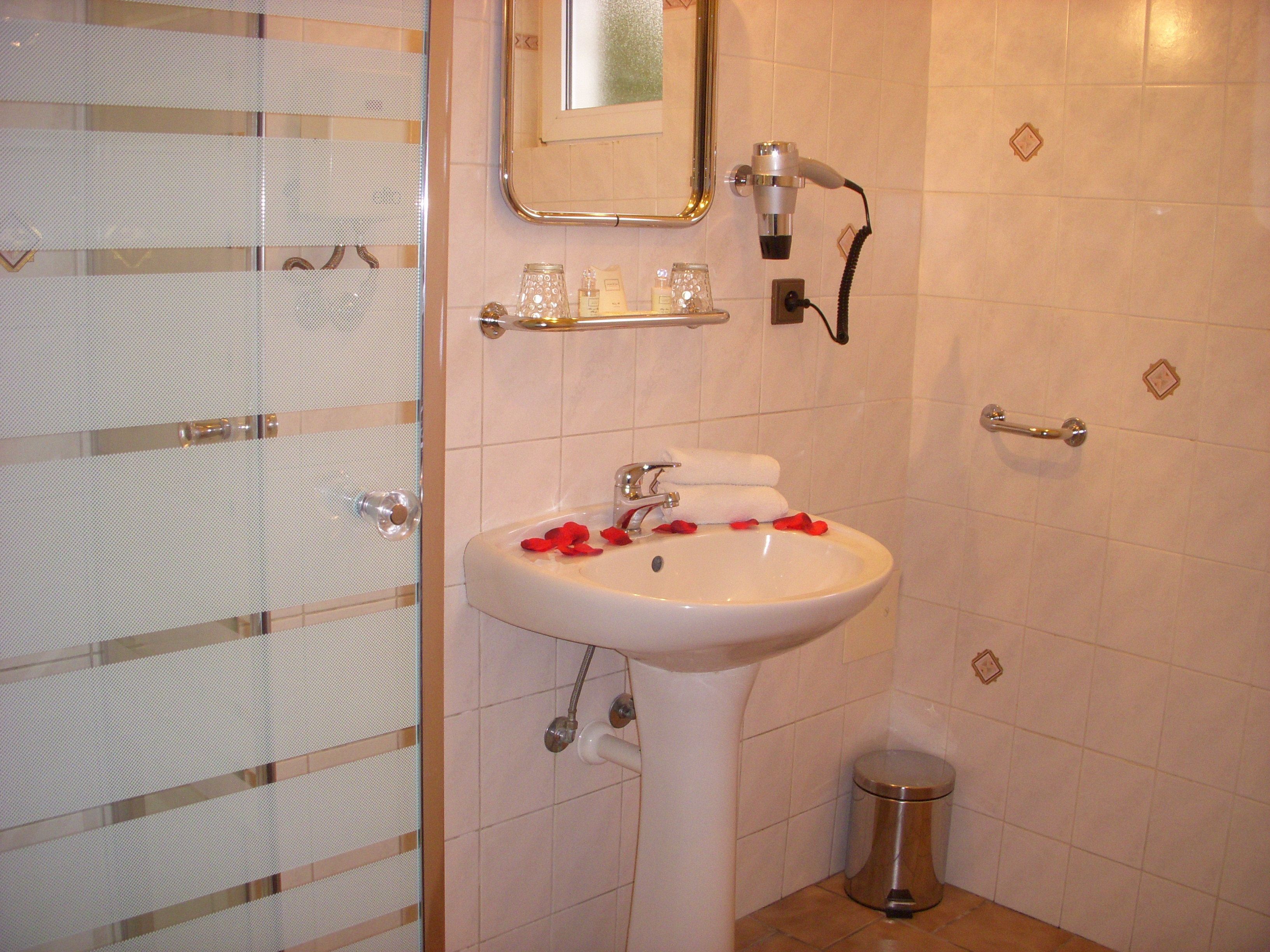Un baño con lavamanos blanco, espejo y zona de ducha.
