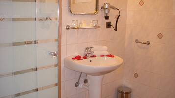 Un baño con lavamanos blanco, espejo y zona de ducha.