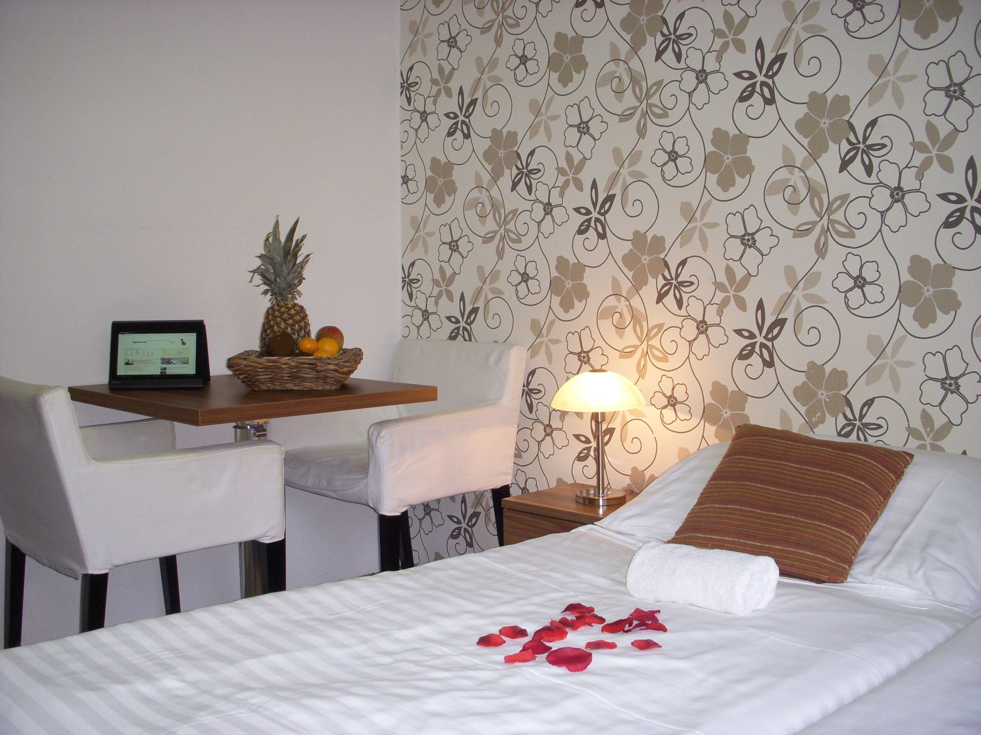 A hotel room with a bed, a desk with a laptop, a fruit basket, and a lamp.
