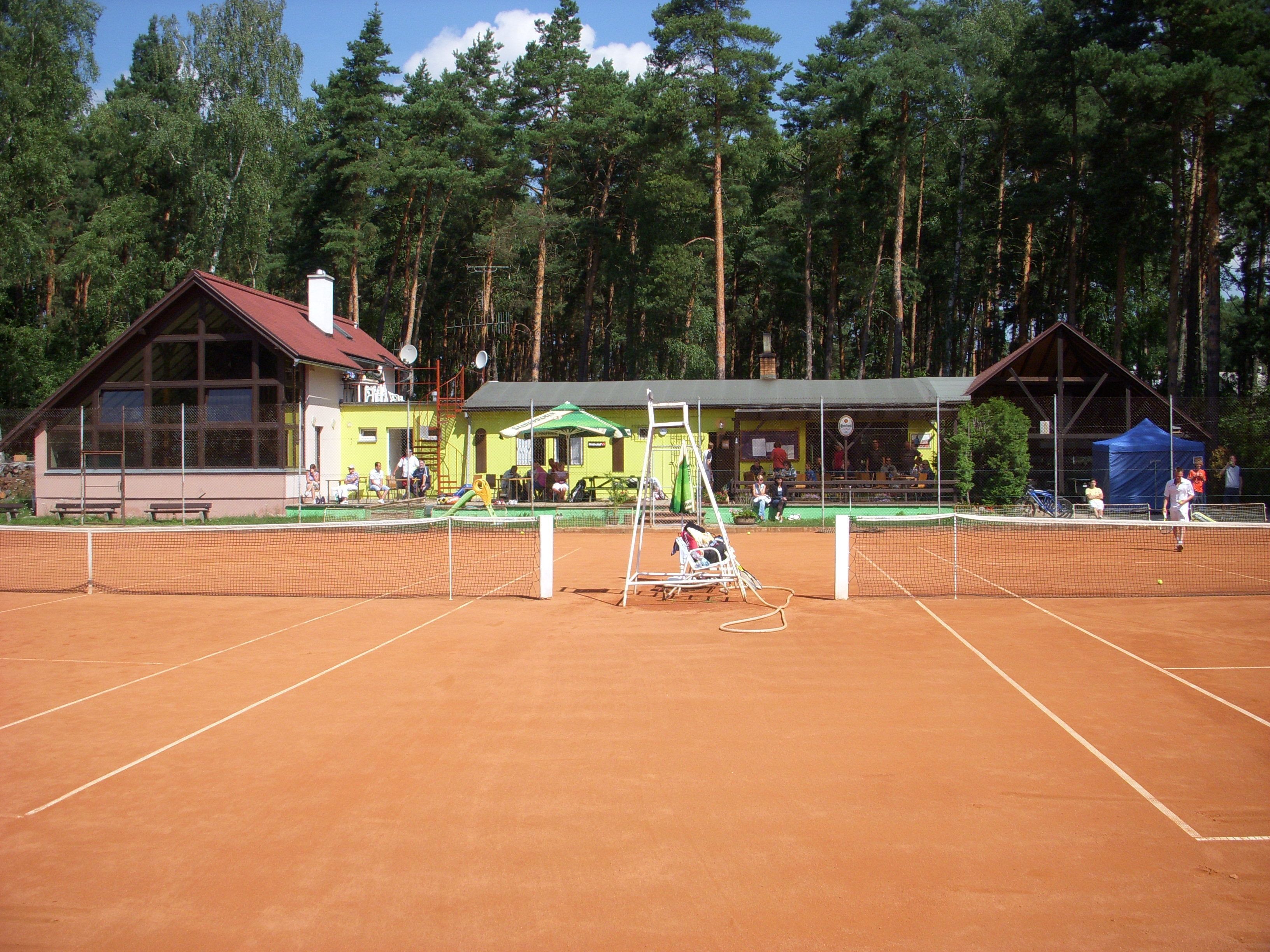 Un court de tennis avec un filet, des bancs et un petit bâtiment doté d’un toit végétalisé.