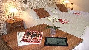 Una habitación de hotel con una cama bien hecha, una mesita de noche con lámpara, una revista y una tableta.