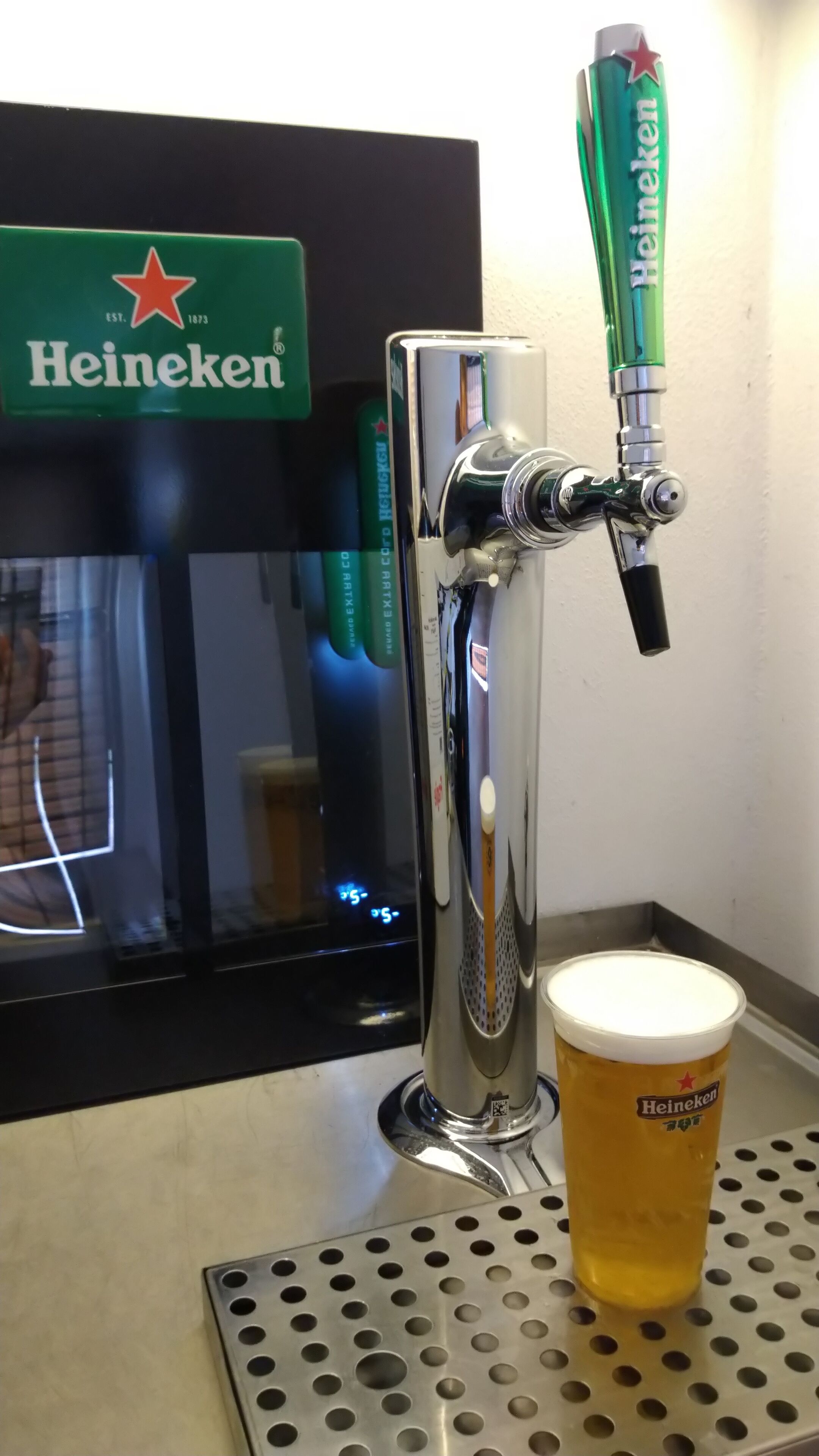 A Heineken tap with a glass of beer on a metal tray.