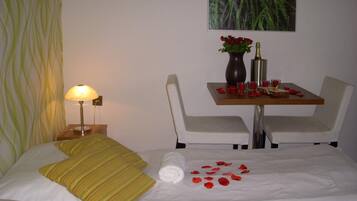 Habitación de hotel con cama, mesita de noche con lámpara, una pequeña mesa con un jarrón de flores y una silla.