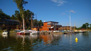 Un puerto deportivo con barcos amarrados, un edificio de madera con balcón, y un cielo azul despejado.