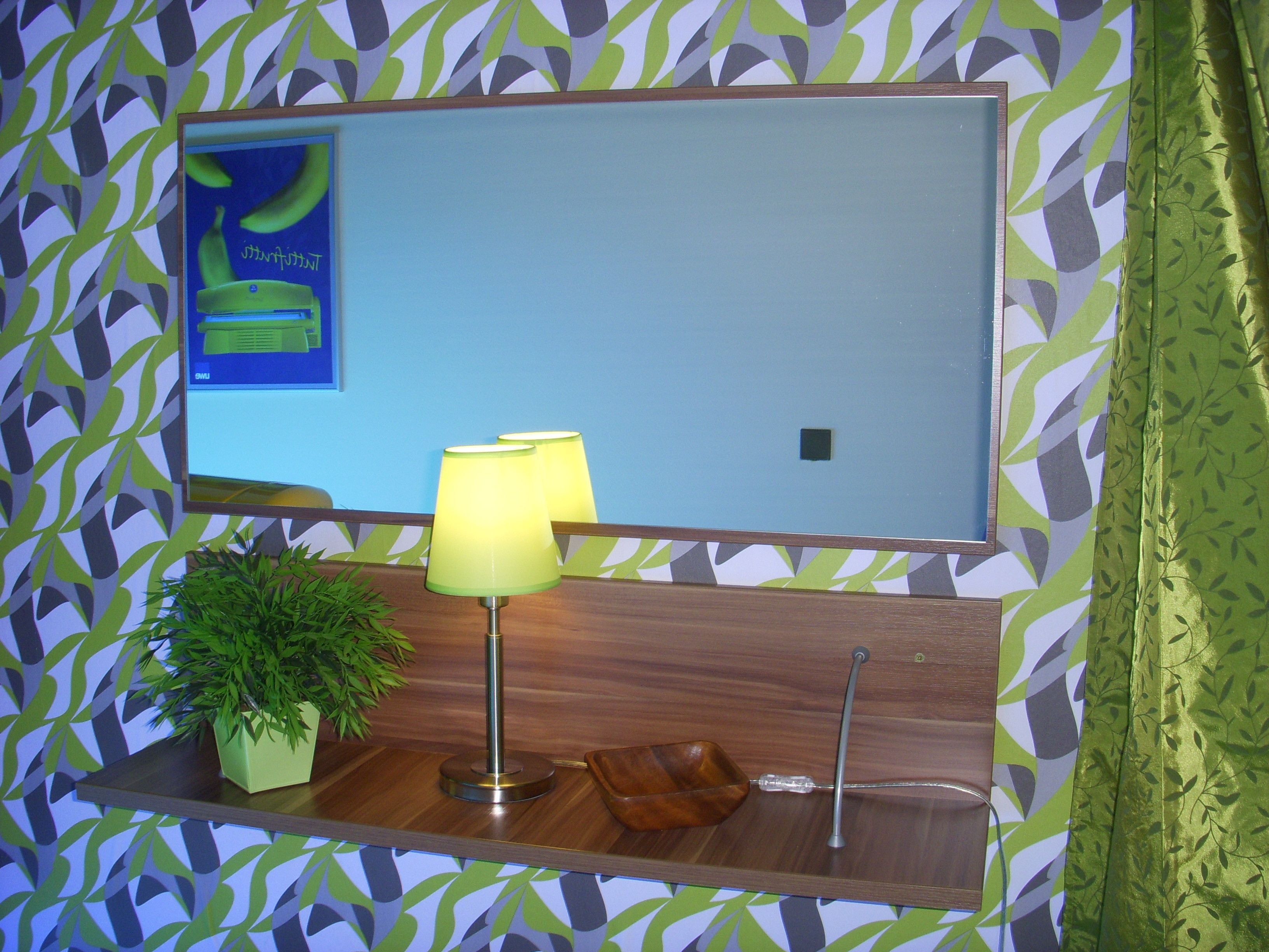 Een aan de muur bevestigde televisie met een bananenreclame, een groene plant en een houten dienblad met een lamp.