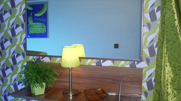 Een aan de muur bevestigde televisie met een bananenreclame, een groene plant en een houten dienblad met een lamp.
