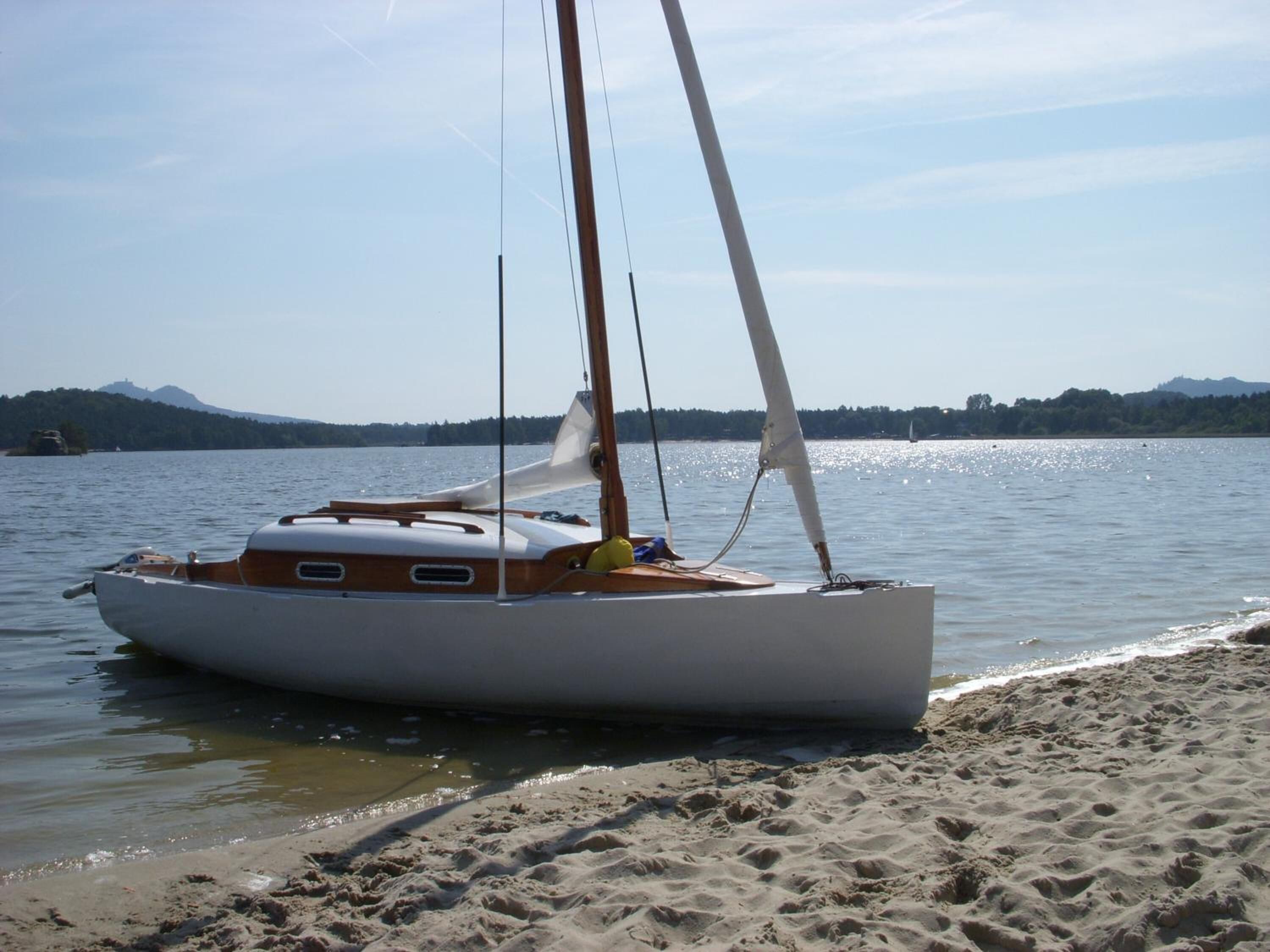 A sailboat docked on a sandy beach with a calm lake and distant mountains.