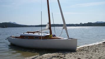 Un velero amarrado en una playa arenosa, con un lago tranquilo y montañas al fondo.