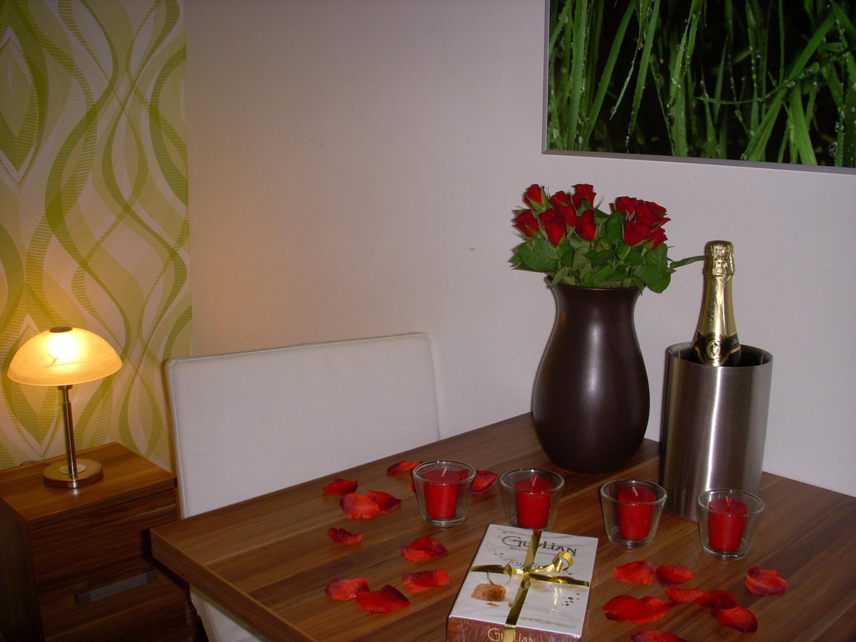 A table with a vase of red roses, a bottle of champagne, and a gift box.