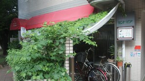 Ein Hotel Eingang mit rotem Markisenvorzelt, ein Fahrrad, das davor abgestellt ist, und ein Schild mit japanischem Text.