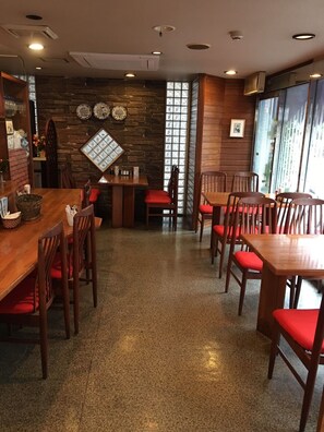 A restaurant with wooden tables and chairs, a stone wall, and a large window with patterned glass. - Hotel Sentpia (Higashimurayama)