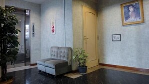 Eine Lobby mit einer grauen Couch, einem Blumentopf, einer Tür und einem gerahmten Bild an der Wand.