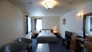 Ein Hotelzimmer mit einem Bett, zwei Sesseln, einem kleinen Tisch, einem Schreibtisch mit Computer, einem Fernseher und einem Spiegel.