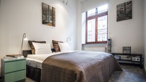 A bedroom with a bed, bedside table, lamp, radiator, and a window with a view of buildings. - Krakow B&B Luxury Old Town (Kraków)