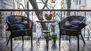 Two wicker chairs with cushions on a wooden deck, a small table with a bottle and a bowl of fruit, and potted plants. - Krakow B&B Luxury Old Town (Kraków)