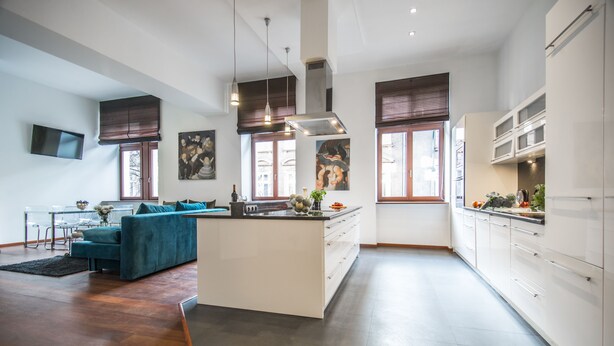 A modern kitchen with a central island, white cabinetry, and a dining area with a blue sofa. - Krakow B&B Luxury Old Town (Kraków)