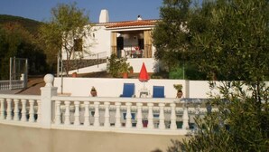 Un bâtiment à deux étages doté d’un balcon, d’un parasol rouge et d’une clôture blanche.