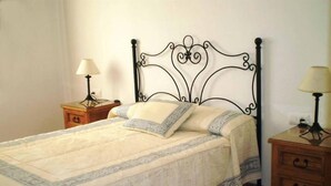 Un lit bien fait, avec une couvre-lit à motifs, une tête de lit décorative en métal et des tables de chevet dotées de lampes et de tiroirs.