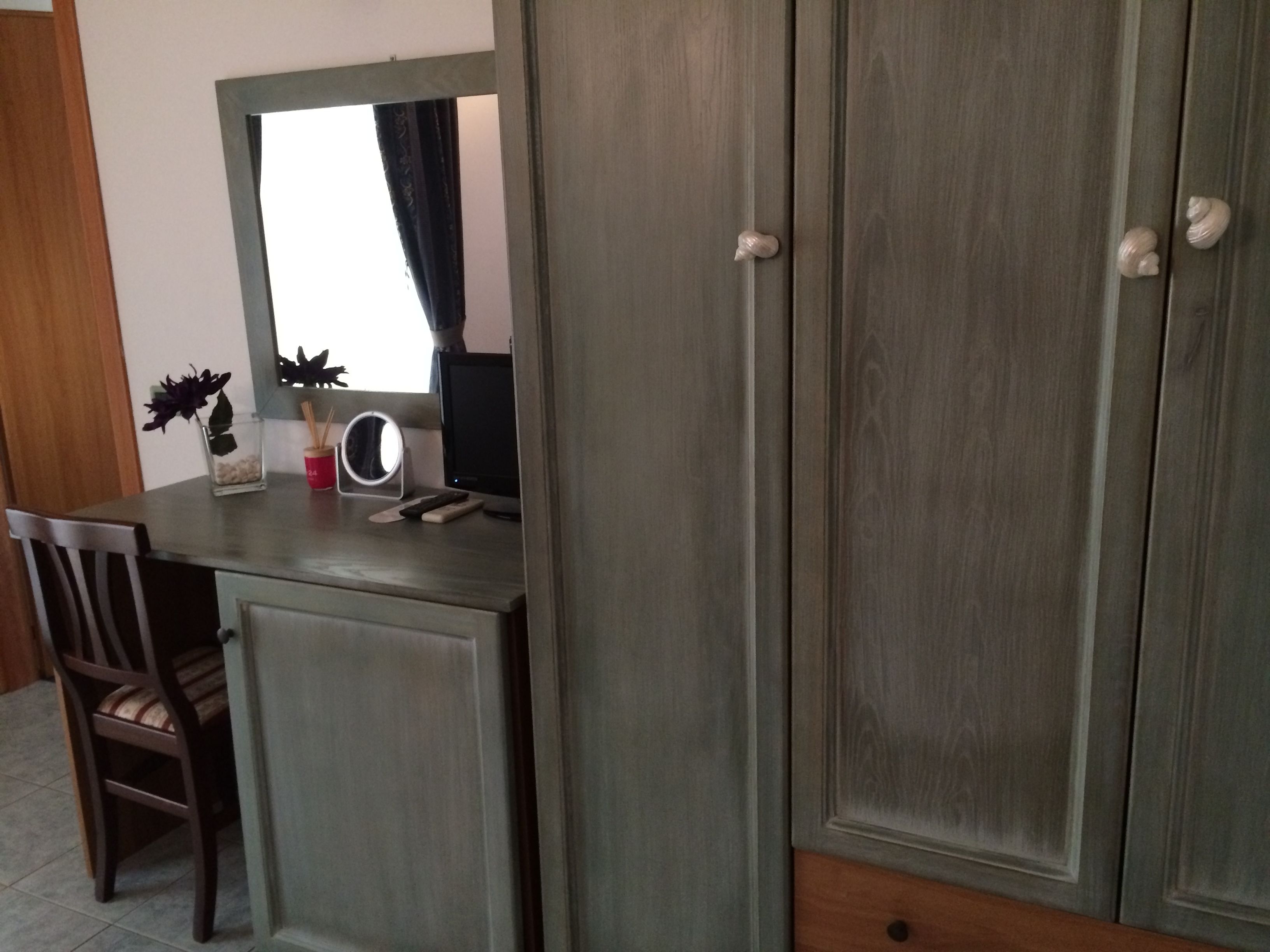 A room with a wooden desk, a chair, a mirror, and a wardrobe.