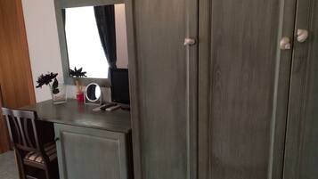 A room with a wooden desk, a chair, a mirror, and a wardrobe.
