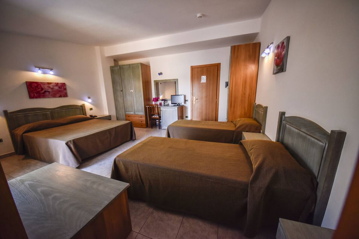 Habitación de hotel con cuatro camas dispuestas en forma de U, un escritorio, una silla y un televisor.