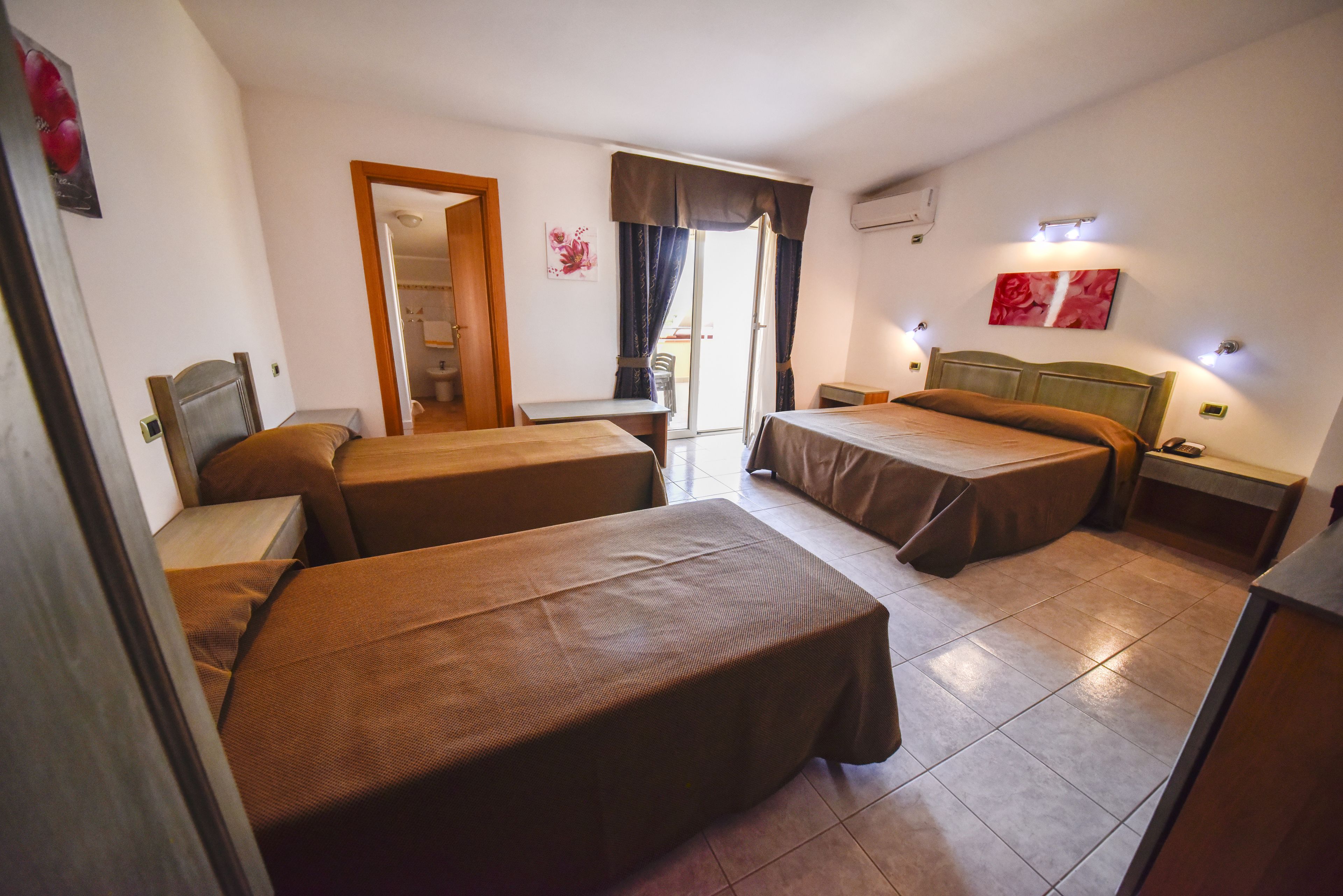 Une chambre d’hôtel avec deux lits simples, une petite table, une chaise, un bureau et une salle de bain visible à travers une porte ouverte.