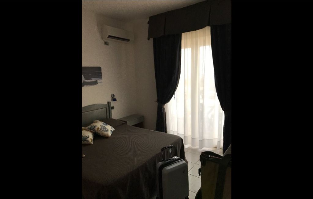 A hotel room with a bed, a suitcase, a chair, and a window with curtains.