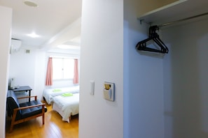 A room with a bed, a desk, and a chair. There is a window with curtains, a wall-mounted air conditioner, and a coat hook. - Hotel Chuo Selene (Osaka)
