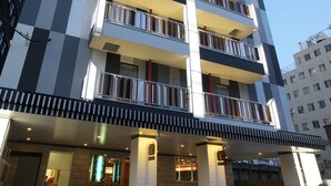 A multi-story hotel with a checkered facade, balconies on each floor, and a covered entrance area. - Hotel Chuo Selene (Osaka)