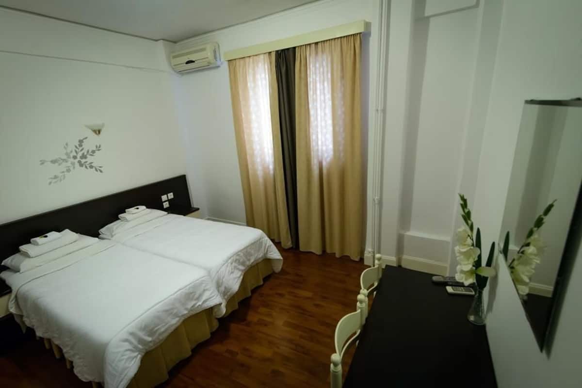 A hotel room with two beds, a desk, a chair, a mirror, and a window with curtains.