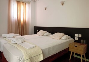 Quarto de hotel com duas camas, uma mesa de cabeceira de madeira e uma janela com cortinas.
