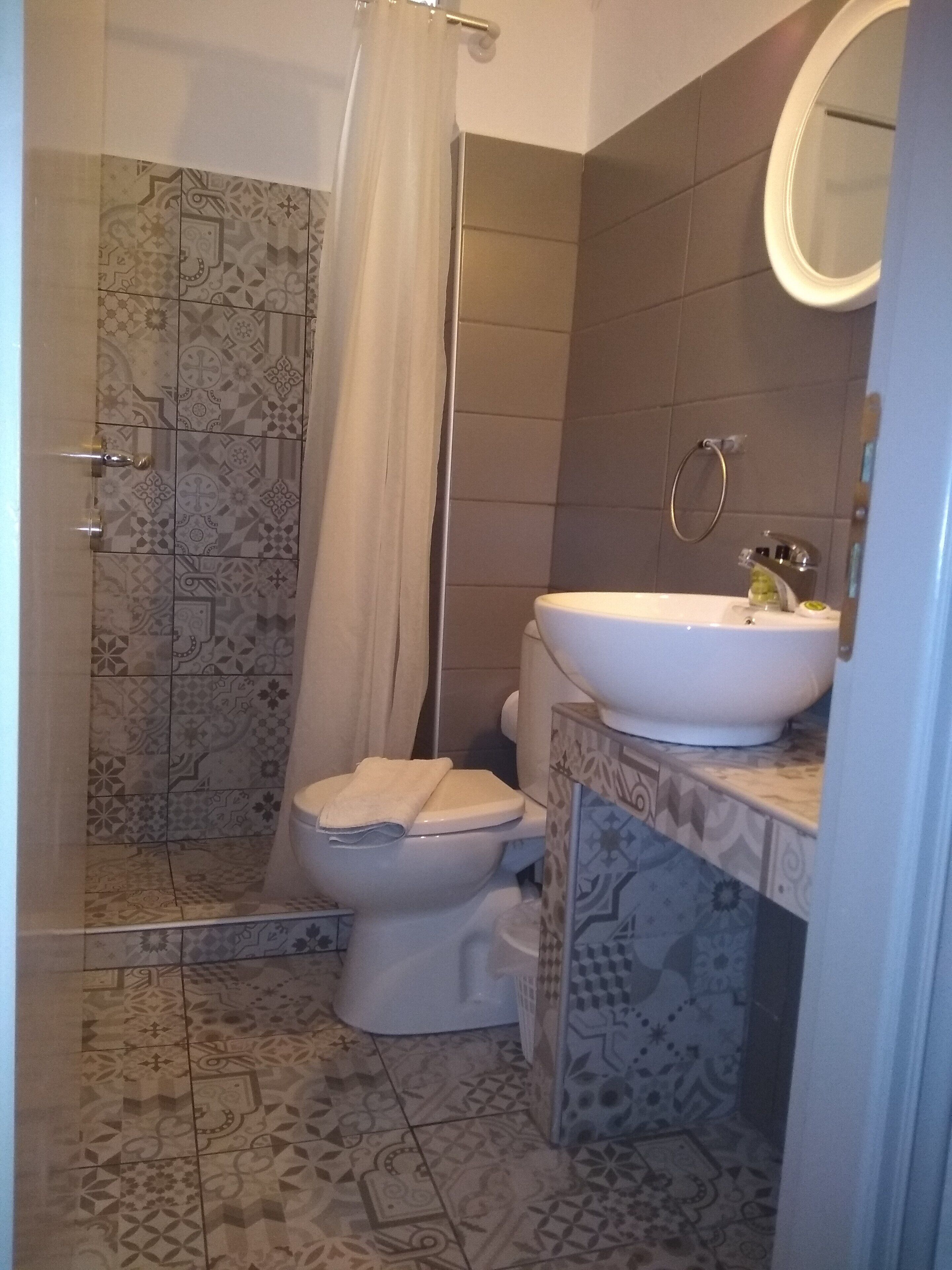 A bathroom with patterned tiles, a shower, a toilet, and a sink with a mirror above it.