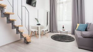 A modern living room with a staircase, a flat-screen TV, a dining table with chairs, a sofa, and a window with curtains.